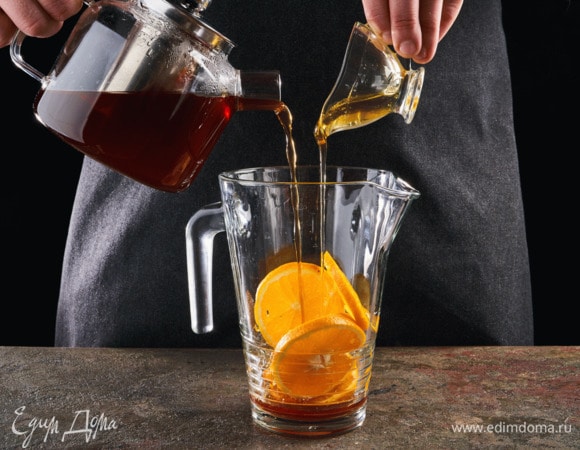 В кувшин добавьте дольки апельсина, залейте черным чаем и медом.