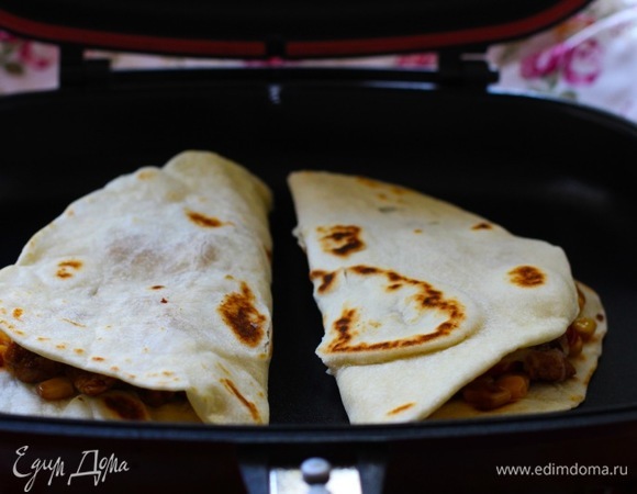 Собрать кесадилью. На лепешку выложить часть начинки, посыпать тертым сыром и сложить пополам, слегка прижав. Повторить то же с оставшимися тортильями.