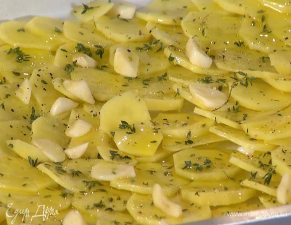 Противень выстелить бумагой для выпечки и выложить картошку в один слой, не накладывая кружки друг на друга, затем полить половиной оливкового масла, посыпать листьями с 4‒5 веточек тимьяна и нарезанным чесноком, посолить и поперчить.