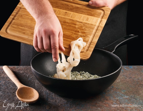 На сковороде в масле обжарьте лук до золотистого цвета. Добавьте кальмаров к луку,