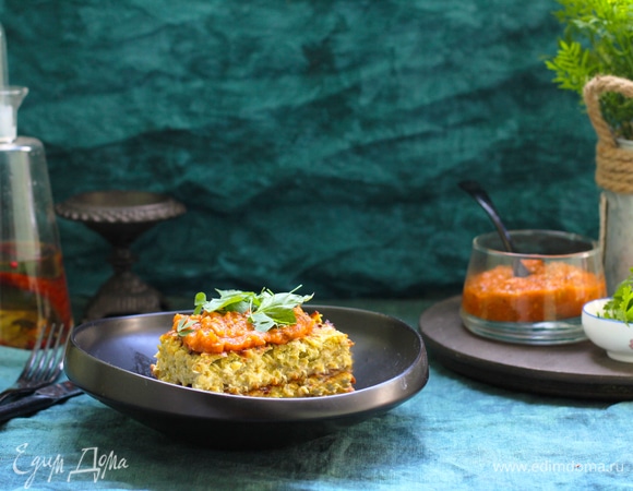 Пока запеканка из кабачков с сыром запекается, приготовьте соус из помидоров. Для этого чеснок очистите и мелко нарежьте. Мелко нарежьте всю пряную зелень. Помидоры бланшируйте в кипящей воде, 2 минуты. Сразу же обдайте холодной, а лучше ледяной, водой и снимите кожицу, сделав надрез крест-накрест внизу помидора. Для запеканки из кабачков выбирайте мясистые помидоры без избытка сока. Разрежьте помидоры пополам, удалите сок и семена. Они для приготовления этого блюда не нужны. Мякоть помидоров нарежьте мелкими кубиками. Луковицу нарежьте таким же образом, как и для запеканки. Обжарьте нарезанный лук на среднем огне с оставшимся оливковым маслом до золотистого цвета, 6–7 минут. Добавьте чеснок, пряные травы, сахар. Посолите и поперчите. Сковороду снимите с огня. Дайте ему настояться, 10–20 минут. Измельчите блендером и охладите до комнатной температуры. Подавайте запеканку теплой или остывшей с соусом.