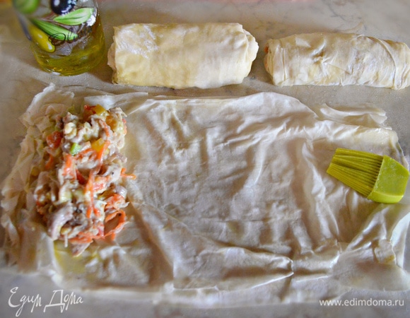 Разложите тесто фило на рабочей поверхности. Каждый лист смажьте растопленным сливочным маслом при помощи кисточки. Сложите стопку из 3–4 листов и разрежьте ее пополам. С краю теста выложите начинку и сверните конвертом, подворачивая края.