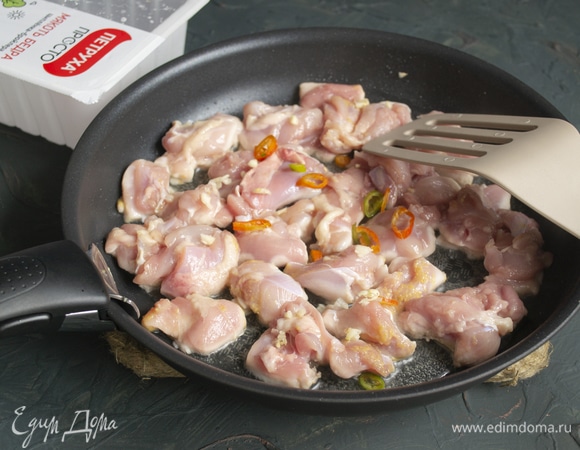 В сковороде смешиваем сливочное и растительное масло, в растопленное масло кладем кусочки курицы, добавляем мелко нарезанный корешок имбиря и чили, посыпаем чесночным порошком. Готовим на сильном огне несколько минут.