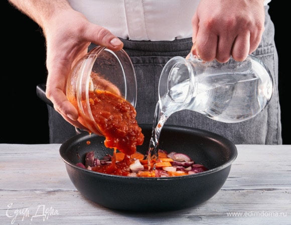 Выложите к луку и моркови томатную пасту, влейте 50 мл воды.