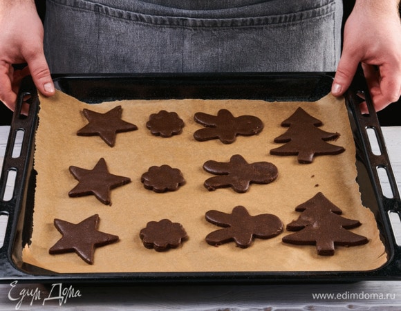 Раскатайте тесто на пекарской бумаге и вырежьте при помощи формочек новогодние фигуры — елочки, звезды, домики. Отправьте в заранее разогретую до 190°C духовку. Выпекайте около 9 минут.