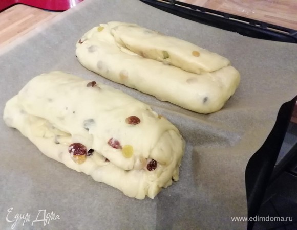 Разделить тесто на 2 части. Раскатать тесто в прямоугольник толщиной 2–3 см и завернуть длинные стороны прямоугольника к середине, чтобы один край находил на другой. Округлить края штоллена руками. Выложить штоллены на противень, накрыть и дать подойти в теплом месте в течение 1 часа.