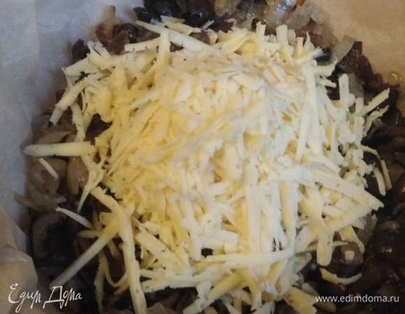 Форму застелить пекарской бумагой. Выложить грибы. Сверху натертый на крупной терке сыр.