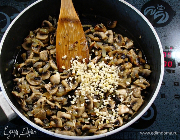 Как только грибы и лук будут готовы, всыпать оставшуюся часть мелко нашинкованного чеснока. Перемешать, посолить, поперчить и слегка обжарить. Снять с огня и слегка остудить.