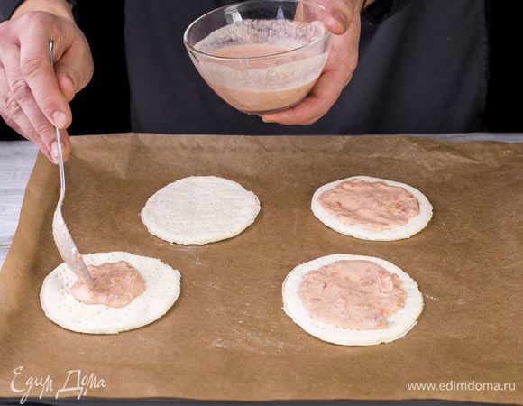 Дрожжевое тесто разморозьте и раскатайте на мини-пиццы. Выложите заготовки на противень, застеленный пергаментной бумагой, и смажьте майонезно-томатным соусом.