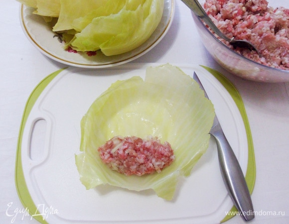 Раскладываем капустный лист на разделочной доске, срезаем толстые стебли до толщины листа. Выкладываем мясную начинку. 