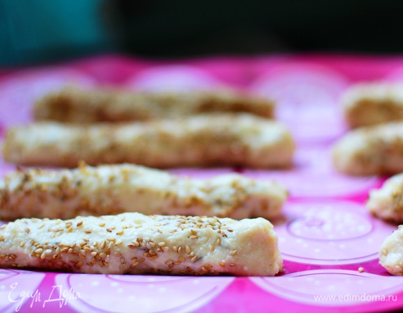 Даем тесту отдохнуть 10–15 минут и нагреваем духовку до 200°C (400°F). Далее формируем хлебные палочки. Отщипываем небольшое количество теста и раскатываем руками по кухонной поверхности. Дело это веселое, поэтому позовите на помощь маленьких помощников. Когда палочка сформирована, высыпаем на стол семена кунжута (не много) и, продолжая формировать палочки, вкатываем семена в тесто.
