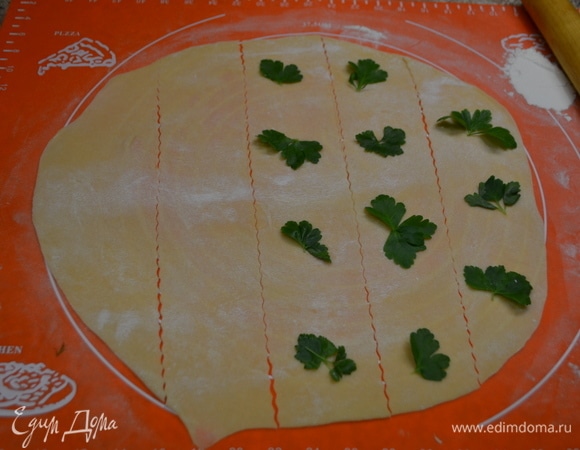 В муку добавляю соль, оливковое масло, яйца, замешиваю тесто. Это долгий процесс. Если желтки оказались недостаточно яркими, можно слегка подкрасить тесто куркумой. Когда тесто станет пластичным, оно готово. На 30 минут убираю его в холодильник. Раскатываю тесто в пласт толщиной 1 мм и нарезаю на полоски. Через полоску выложить листочки зелени так, как показано на фото.