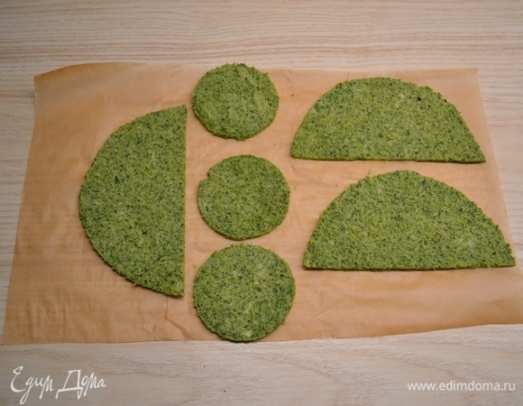 Первым делом необходимо приготовить бисквит. Белки отделить от желтков. Соединить желтки, шпинат, соль и муку. Пробить блендером до однородного состояния. Белки взбить со щепоткой соли в пышную массу и ввести лопаткой в тесто. Пергамент смазать растительным маслом, вылить тесто и разровнять. Выпекать 8–10 минут при 180°C. Снять с пергамента и вырезать заготовки для елочек.