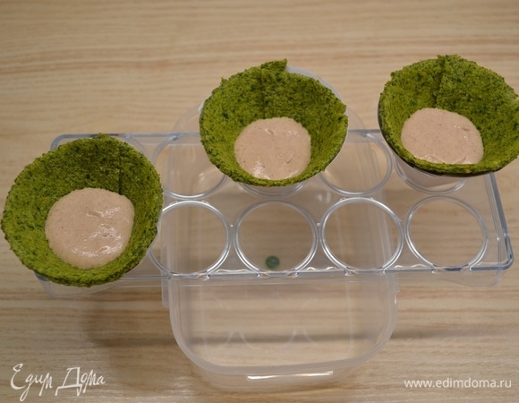 Для того чтобы собрать елочки, очень удобно воспользоваться подставкой под яйца. Установить подставку сверху на контейнер. В дырочки вложить конусы из бумаги. В каждый конус вложить заготовку из теста. Наполнить конус наполовину муссом из печени, затем добавить 1 столовую ложку клюквенного пюре и сверху опять заполнить муссом. 