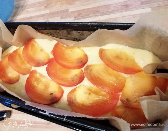 Форму для кекса смазать маслом и посыпать мукой или манкой или выстлать пергаментной бумагой. Вылить тесто, оно относительно жидкое. Сверху разложить тонко нарезанные ломтики хурмы. Вместо хурмы можно использовать ломтики апельсина.