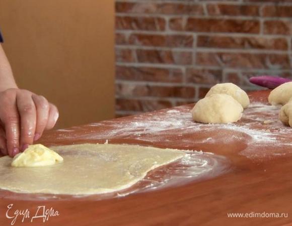 Выкладываем тесто. Делим на кусочки по 100 г. Обминаем. Размазываем по столу сливочное масло. Равномерно растягиваем кусочек теста руками. Сверху смазываем сливочным маслом. Выкладываем крем. Заворачиваем в рулетик. После — в улитку. Повторяем так с каждым кусочком теста. Покрываем противень пергаментом. Выкладываем булочки.
