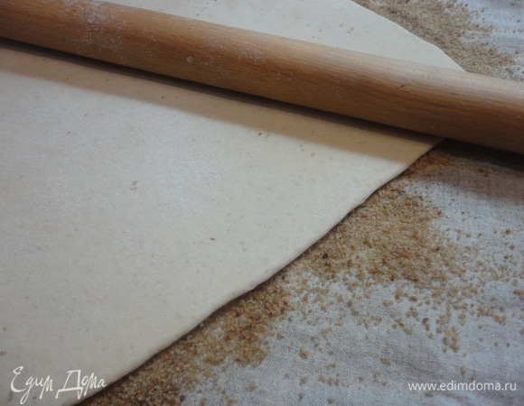 Затем достать тесто из морозильной камеры. Поверхность теста слегка смочить водой и перевернуть на сухари. Сверху слегка прокатать скалкой.