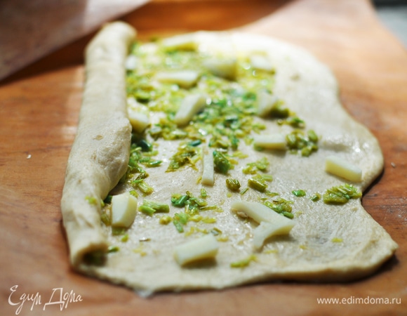 Тесто разделить на 3 равные части (вес каждой — примерно 230–250 г). Каждую раскатать на подпыленном мукой столе на прямоугольные заготовки в соответствии с размером кексовой формы (у меня форма длиной 32 см). Намазать на пласт треть обжаренных стрелок, можно добавить немного сыра. Скатать пласт в рулет. Так же поступить и с остальными двумя кусками теста. Из трех рулетов сплести косу, положить заготовку в смазанную форму, края подоткнуть. Можно выпекать на противне, но тогда хала будет широкой и низкой.