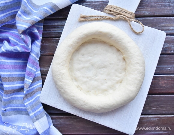 Должна получиться заготовка с тонким слоем теста в середине и толстыми округлыми краями. Оставить их в теплом месте, накрыв салфеткой еще на полчаса.
