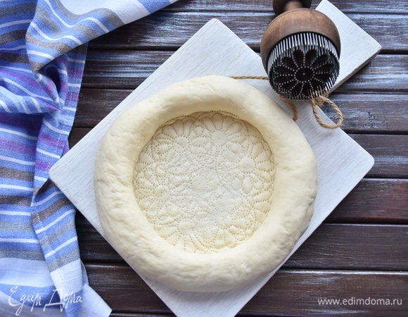 С помощью специального устройства — чекича — в центре лепешки сделать узор. Можно воспользоваться и обычной вилкой. Смазать хлеб яичным желтком и посыпать кунжутным семенем. Выпекать в духовке, разогретой до 220–230°C, до аппетитной корочки.