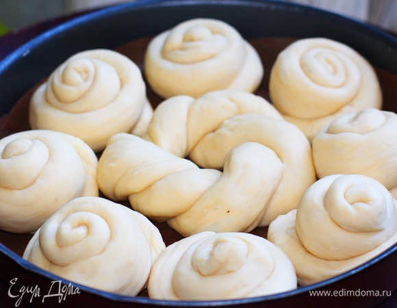 Из всех шариков сделать жгуты. Два из них скрутить между собой и сделать «венок» для центра погачи. Выложить его в центр застеленной бумагой или смазанной маслом формы диаметром 26–28 см. Остальные жгуты скрутить улиткой, хвостики спрятать под заготовку, расставить заготовки в форме вокруг «венка». Накрыть полотенцем и дать подойти 20 минут. Смазать верх молочно-желтковой смесью. По желанию густо посыпать кунжутом или маком.