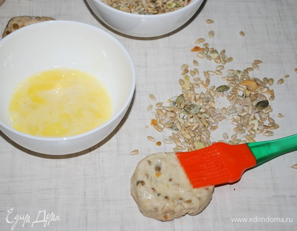 Сформируйте булочки, смажьте поверхность яйцом, посыпьте оставшимися семечками и слегка вдавите их в тесто.