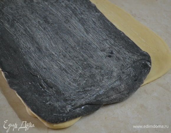 Для формовки тесто раскатываем, как можно тоньше. Получается два разных по цвету пласта теста. Стараемся, чтобы пласт белого теста был немного больше, чем черный. Смазываем белый пласт теста растопленным маслом, оставляя края на 1–1,5см без масла. Сверху кладем прямоугольник из черного теста. Один край плотно защипываем.