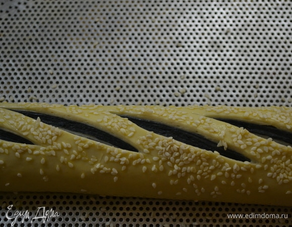 Переносим на противень. Верх багета смазываем взбитым яйцом и посыпаем кунжутом. Делаем разрезы. Противень с заготовками накрываем пленкой и ставим на расстойку на 30 минут.