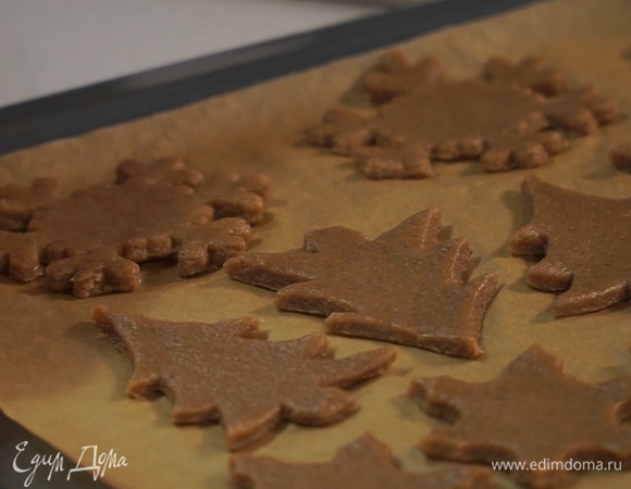 При помощи формочек для печенья вырезать из теста фигуры, выложить их на застеленный пергаментом противень. В фигурках сделать маленькие отверстия для веревочек. Выпекать в духовке при 180°С в течение 12 минут.