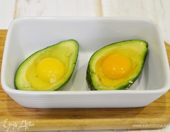 Аккуратно, не повредив желток, вбейте по яйцу в каждую половинку авокадо.