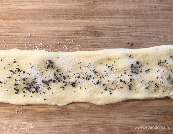 Каждый шарик раскатать в небольшой пласт руками или скалкой, смазать маслом, посыпать сахаром и маком, свернуть в рулет.