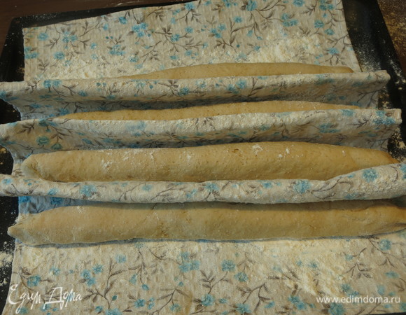 Растягиваем заготовки багетов и выкладываем на полотенце, присыпанное мукой, предварительно сформировав бортики.