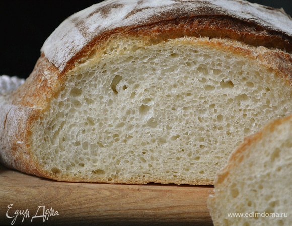 Духовку включить на 230°C за 45 минут до начала выпечки. Перед выпечкой заготовку перевернуть на лопату швом вниз. По желанию украсить трафаретом и сделать разрезы. Выпекать первые 20 минут под колпаком. Затем колпак снять и продолжить печь еще 15 минут. Готовый хлеб охладить на решетке.