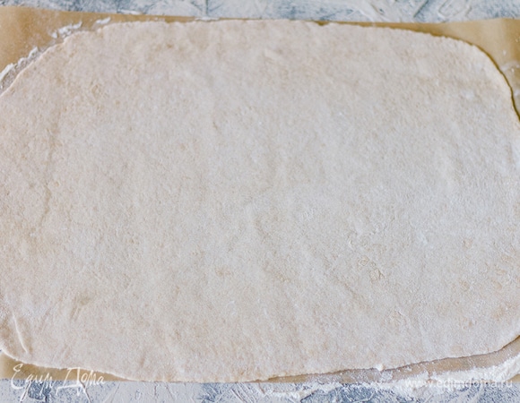 Поднявшееся тесто обмять и на пергаменте раскатать тонким слоем в прямоугольник.