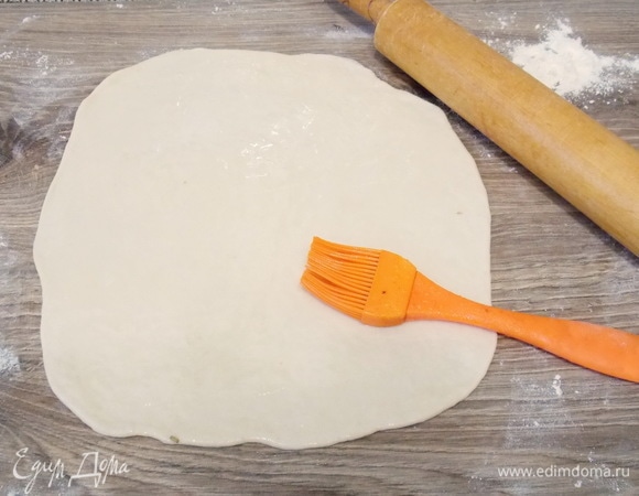 Теперь стол посыпаем немного мукой и раскатываем каждый шарик в тонкий пласт. Смазываем их 1 столовой ложкой масла.