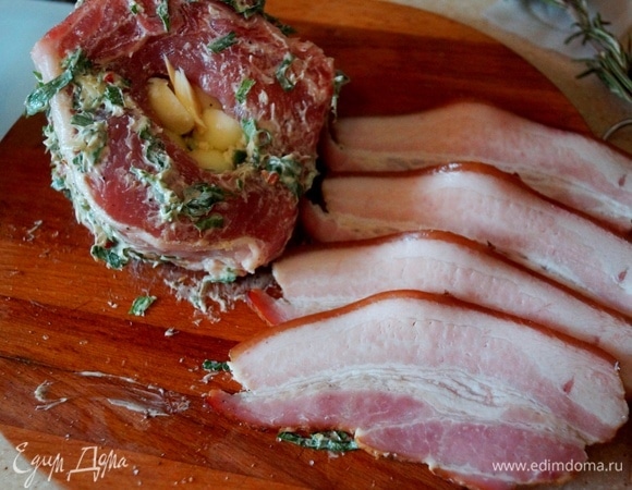 Натираем корейку солью, перцем и пряным маслом. Делаем разрез посередине и фаршируем кусочками сыра. Заворачиваем мясо в бекон и кладем на противень, смазанный маслом.