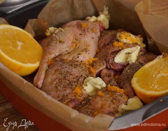 Утиные ножки уложить в глубокий противень, выстеленный бумагой для выпечки, посыпать гвоздикой, кориандром, молотым перцем, солью и цедрой, рядом поместить половинки апельсина, полить все 1‒2 ст. ложками оливкового масла, сверху разложить кусочки сливочного масла.