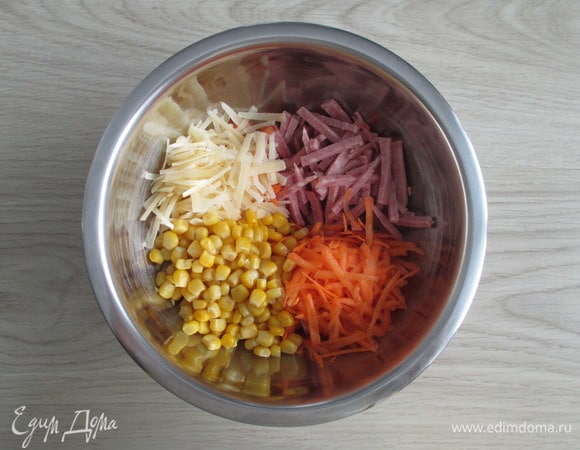 Из банки с консервированной кукурузой слейте жидкость. Сырую морковь натрите крупно, так же натрите полутвердый сыр. Колбасу нарежьте соломкой.
