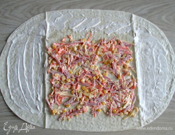 Края лаваша, которые будут подгибаться, слегка смажьте майонезом по вкусу. По центру разложите яркую начинку. Скрутите рулет.