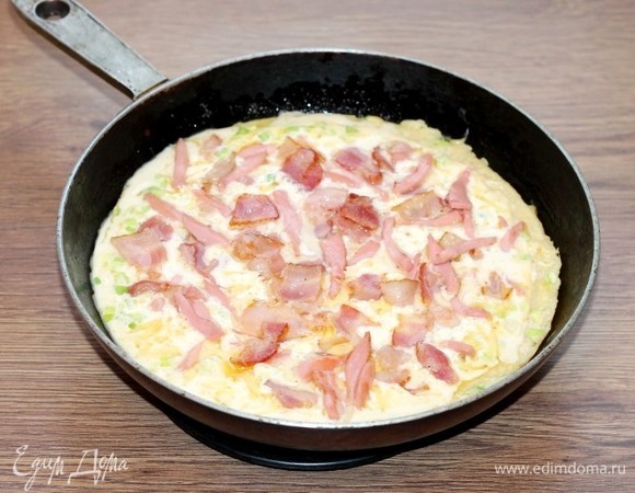 Сверху на пирог выложить обжаренный бекон (и колбасу). Отправить сковороду с блюдом в разогретую до температуры 180-190°C духовку на 20 минут.