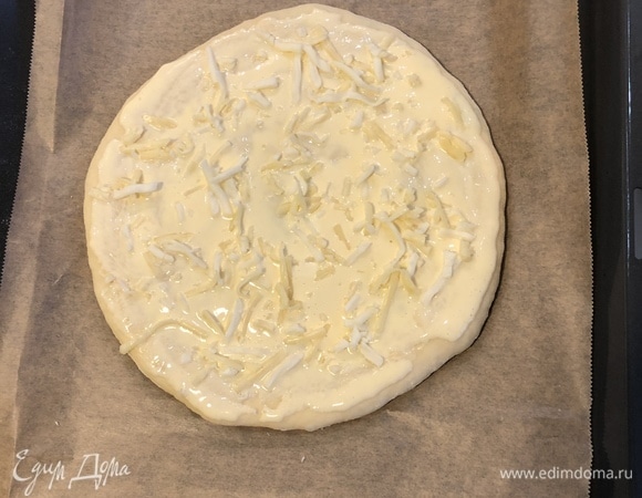 Руками очень осторожно раскатать закрытую лепешку. В отдельной миске соединить сметану и желток, смазать этим лепешку, посыпать сыром.