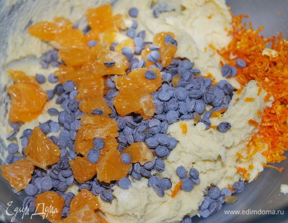 В тесто добавьте шоколадные капли (у меня горький шоколад), мандарин, очищенный от пленок и нарезанный на мелкие кусочки, а также цедру мандарина по желанию (у меня одна чайная ложка цедры). Все перемешайте.