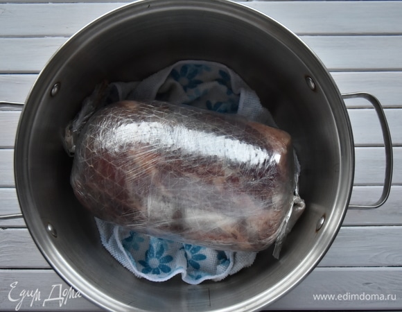 На дно кастрюли уложить тканевую салфетку, чтобы полуфабрикат не соприкасался с дном кастрюли, влить воду и выложить подготовленное мясо. Поставить кастрюлю на огонь, довести до кипения. Огонь уменьшить до самого минимального. Вода не должна кипеть. Кастрюлю крышкой не накрывать.Можно приподнять кастрюлю над огнем с помощью подставки. Температура воды должна быть не более 80°C. Как только температура внутри куска мяса достигнет 69°C, можно снимать его с огня — ветчина готова. При отсутствии термометра ориентироваться по времени. На варку достаточно крупного куска мяса ушло 3 часа. Ветчину достать из кастрюли, дать полностью остыть, освободить от оболочки и завернуть в пергамент. Перед подачей мясу желательно настояться часов 12 в холодильнике.