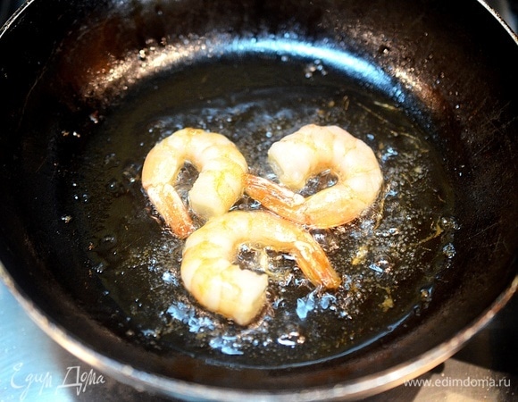 Тем временем разморозьте крупные креветки и обжарьте их на сковороде с добавлением масла.