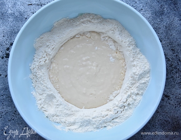 Добавляя постепенно с краев воронки муку, замесить тесто. Когда мука полностью впитает влагу, выложить тесто на рабочую поверхность и продолжить замес.