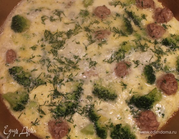 Сковороду немножко смазываем сливочным маслом, выкладываем брокколи и фрикадельки. Все заливаем молочно-яичной смесью. Сверху посыпаем мелко нарезанным укропом. Прикрываем крышкой и готовим 5 минут. Блюдо готово! Для подачи можно использовать свежие овощи и хлеб. Приятного аппетита.