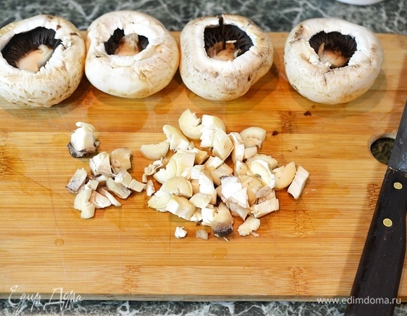 Аккуратно удалите ножки у грибов, стараясь не повредить шляпки. Нарежьте ножки грибов кубиком.