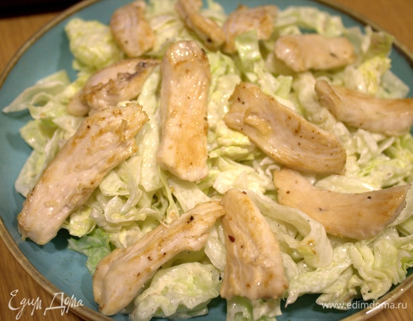 На дно плоской тарелки перенести салат с заправкой, сверху — кусочки курицы.