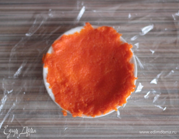 Блюдце застелить кусочком пищевой пленки, аккуратно выложить ложку натертой моркови и разровнять. Стараться, чтобы не было дырочек и получилась как бы тонкая лепешка.