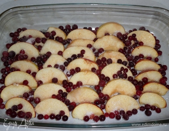 В большую глубокую форму для запекания выкладываем нарезанные ломтики яблок. Добавляем ягоды клюквы. Затем добавляем сахар и 1/2 ст. л. соли.